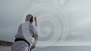 Sporty man practicing karate fighting on beach. Bearded athlete workout outdoors