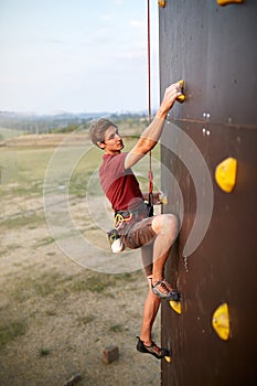 Sporty man practicing rock climbing in gym on artificial rock training wall outdoors. Young talanted climber guy on