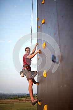 Sporty man practicing rock climbing in gym on artificial rock training wall outdoors. Young talanted climber guy on