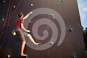 Sporty man practicing rock climbing in gym on artificial rock training wall outdoors. Young talanted slim climber guy on