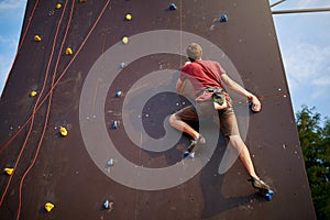 Sporty man practicing rock climbing in gym on artificial rock training wall outdoors. Young talanted slim climber guy on