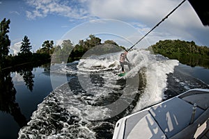 Sporty man rides on wakesurf through the waves on water board photo