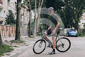 Sporty man standing with black bike on city street