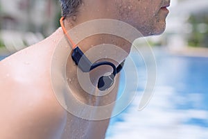 A sporty man in a swimming pool, equipped with waterproof headphones featuring bone conduction technology. Sports and