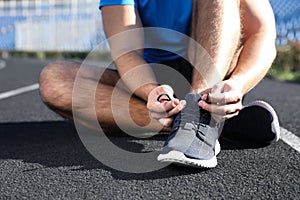 Sporty man tying shoelaces at stadium on sunny morning, closeup