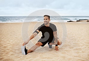Sporty man warming up before jogging outdoors on ocean beach, preparing for fitness workout outside, free space
