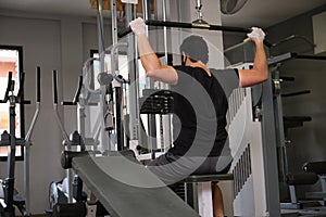 Sporty man wearing protective face mask exercising with lat pulldown machine to build arm and shoulder muscle in fitness gym