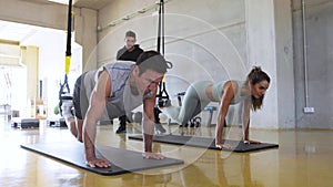 Sporty man and woman training legs and abs with trx fitness straps in the gym.