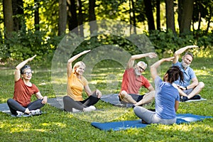 Sporty mature people doing stretching exercises during group training with instructor outdoors