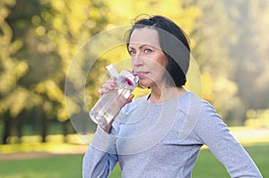 Sporty mature woman drinking water outdoor on sunny day in the park