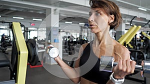 Sporty mature woman is making biceps exercise with dumbbells in gym.