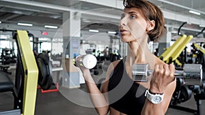 Sporty mature woman is making biceps exercise with dumbbells in gym.
