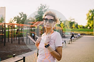 Sporty mature woman posing with a skipping rope in an outdoor sports field. Senior woman holding skipping rope, portrait