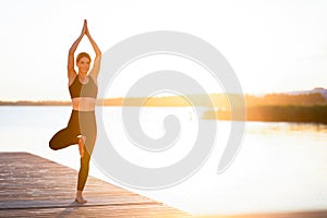 Sporty middle aged female practicing yoga on a wooden pier on sunset