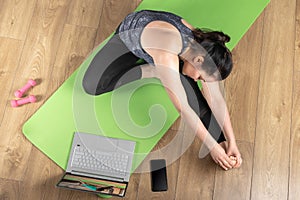 Sporty middle-aged woman making yoga fitness stretching at home via laptop. woman losing weight by online gym workout using