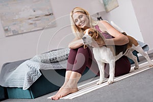 sporty middle aged woman stroking dog while sitting on yoga mat