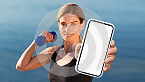 Sporty Middle Aged Woman Training With Dumbbells Outdoors And Showing Blank Smartphone photo