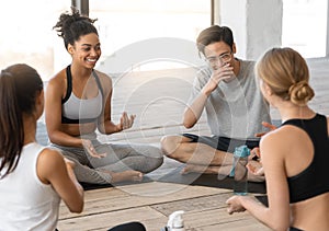 Sporty multicultural men and women sitting on mats, chatting after yoga class