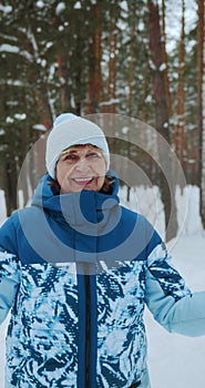 A sporty pensioner looks at the camera while walking through a winter forest