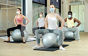 Sporty people in protective masks exercising on pilates balls in gym