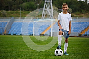 A sporty player with a football ball under his foot on a green grass on a stadium background. Hobby, activities concept.