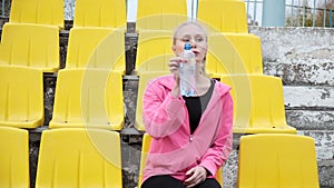 Sporty pretty female sits at staduim tribune, drinks water from plastic bottle