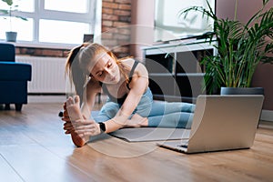 Sporty redhead young woman working out, doing stretching exercise watching fitness video online.