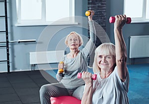 Sporty retired women doing exercises with dumbbells at fitness club