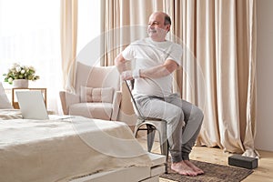 Sporty senior man practicing yoga using chair, doing Parivrtta Utkatasana