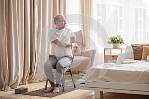 Sporty senior man practicing yoga using chair, doing Parivrtta Utkatasana