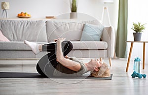 Sporty senior woman doing exercises on yoga mat indoors, blank space