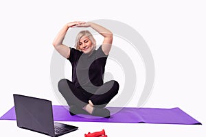Sporty senior woman warming up stretching watching fitness video tutorial on laptop, fit woman doing workout at home sitting on