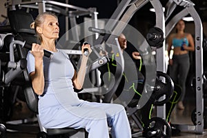 Sporty senior woman working out shoulders muscles on exercise machine