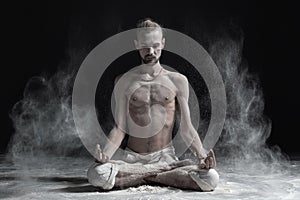 Sporty serene young man meditating sitting in cross-legged yoga lotus pose, Padmasana with palms in mudra