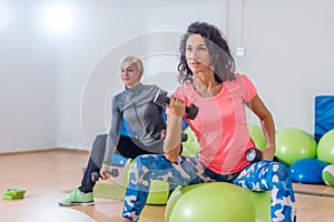 Sporty slim women taking part in gym fitness class exercising sitting on physioballs doing alternated biceps curl with