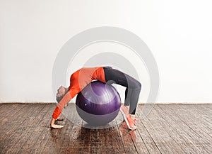 Sporty slim young woman in tight sportswear bending over big fitness rubber ball, stretching and exercising abdomen muscles