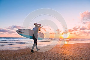 Sporty surf girl go to surfing. Woman with surfboard and sunset or sunrise on ocean