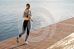 Sporty Woman In Activewear Running Outdoors On Wooden Pier Near River