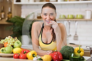 Sporty woman biting cherry tomato at home kitchen