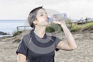 Sporty woman brunette drinking water in a beach.