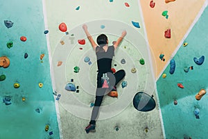 Sporty woman climbing up on practice rock wall indoor