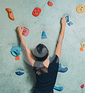 Sporty woman climbing up on rock wall indoor