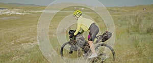 The sporty woman cyclist on bike rides down the field. The girl traveler journey on gravel touring bike with bikepacking