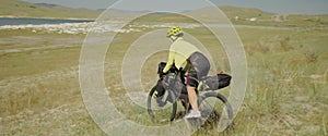 The sporty woman cyclist on bike rides down the field. The girl traveler journey on gravel touring bike with bikepacking