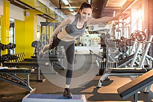 Sporty woman doing balance exercise on one leg on fitness stepper at gym