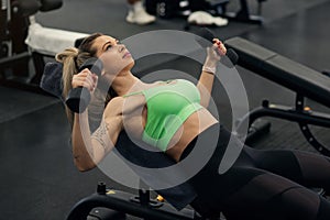 Sporty woman doing dumbbell chest fly lying on bench in the gym.