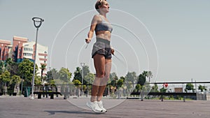 Sporty woman doing jump exercise with skipping rope outdoors. Young female jumping on skipping rope at sports ground