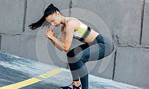 Sporty woman doing squat exercises outdoors. Fit female in modern sportswear exercising outside on the urban concrete walls