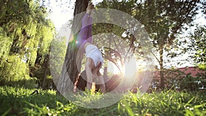 Sporty woman doing yoga exercises with handstand headfirst near the tree.