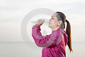 Sporty woman drinking water outdoor on the beach during sunset